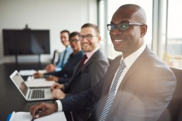 Smiling confident African businessman in a meeting with a group of multiracial co-workers seated at a conference table in the office.